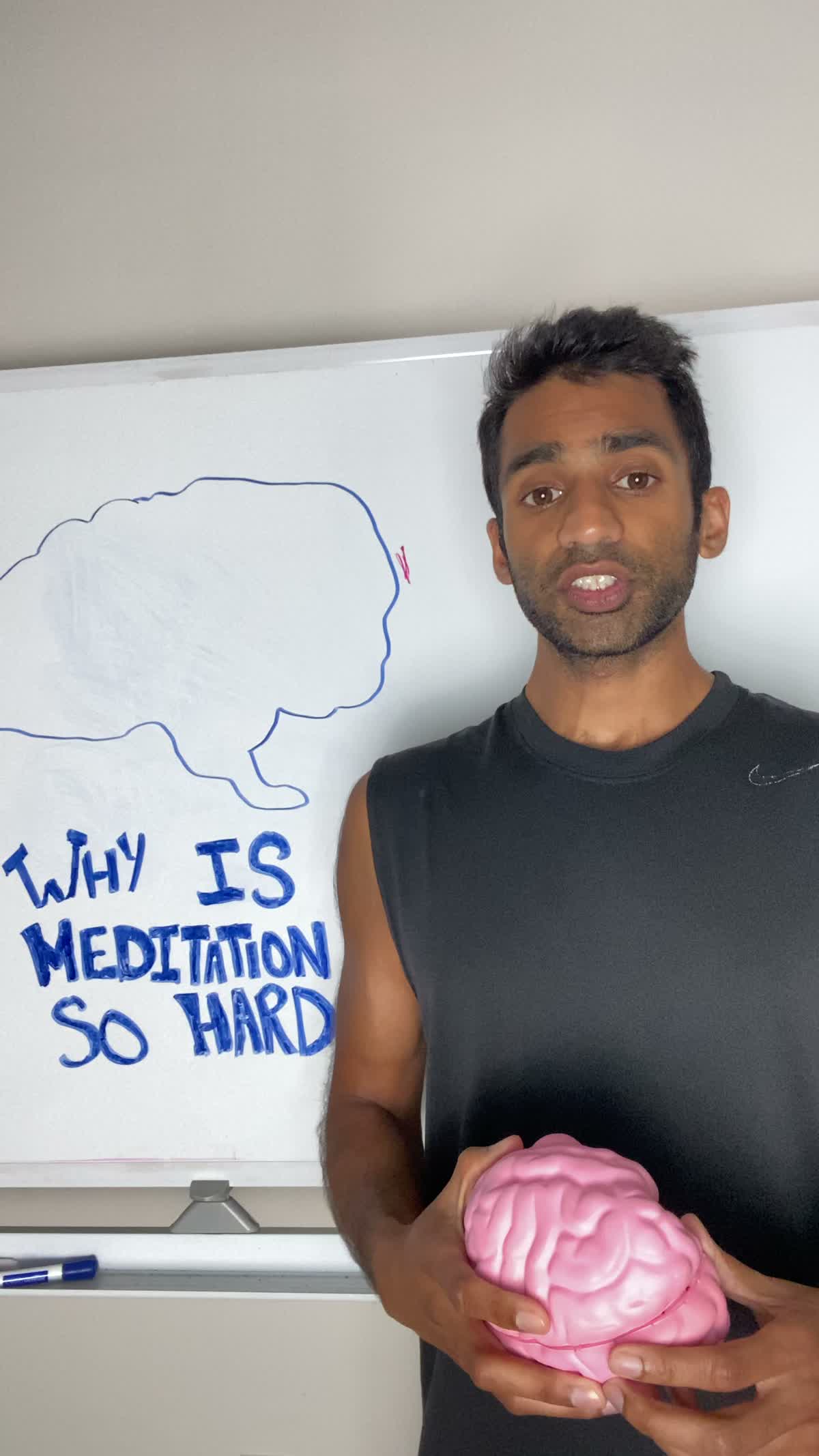 A vertical phone image of Jai mid-sentence holding a pink model brain beside a hand-drawn board asking why meditation is so hard.